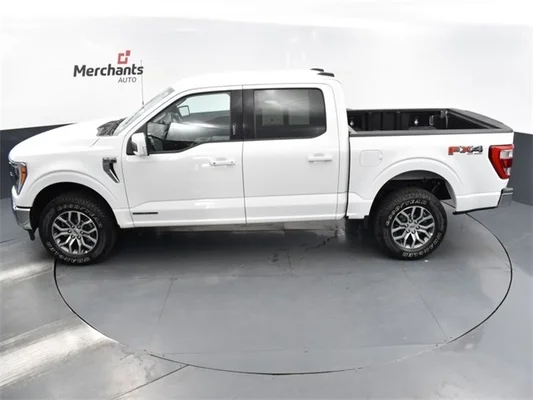A white Ford F-150 pickup truck in a room with a black floor with a white wall with the Merchants Auto logo.