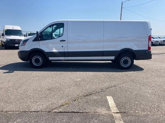 A white Ford Transit cargo van in an asphalt parking lot with a blue sky in the background.